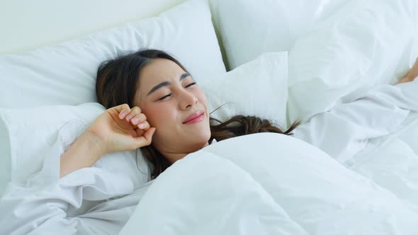 Attractive young woman lying down on bed feel happy with cozy pillow and blanket enjoy early morning