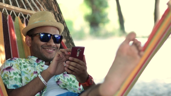 Young Man Swinging In a Hammock While Using Phone