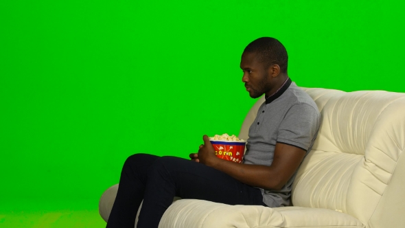 Man With Dark Skin Watching TV And Eating Popcorn. Green Screen