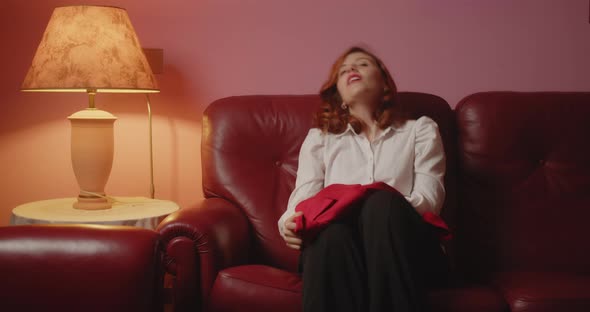 Beautiful girl takes off her red jacket and sits down on the sofa as soon as she returns from work