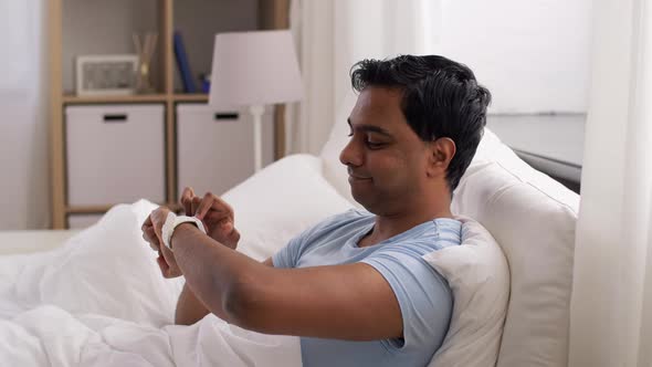 Happy Indian Man with Smart Watch in Bed at Home