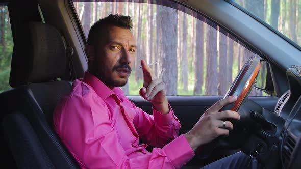 Businessman Smoking a Cigarette While Driving Looking at the Camera and Talking