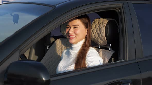 Excited Young Woman in White Pullover Sits in Black Car