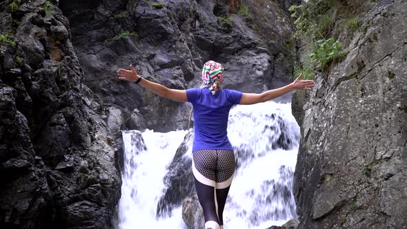 A Woman Stands Against the Background of a Waterfall