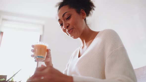 Smiling African pregnant woman holding glass of juice and looking at phone