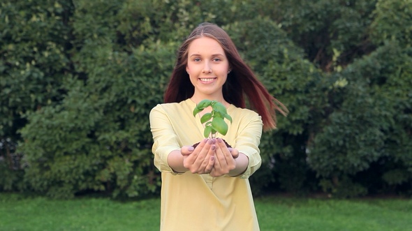 Young Woman Giving Green Young Plant With a Smile
