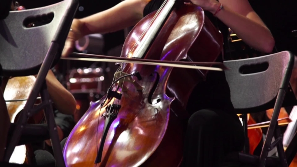 Concert, a Woman Musician Playing The Cello On Stage With a Lot Of Colleagues.