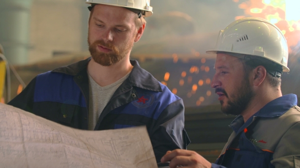 Portrait Of Two Serious Engineers Explore Project In Heavy Industry Factory. Welding Background