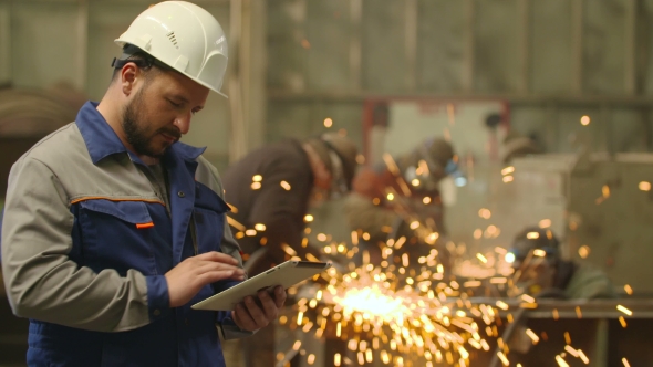 Engineer Using Tablet PC In In Heavy Industry Factory. Grinding Sparks Background