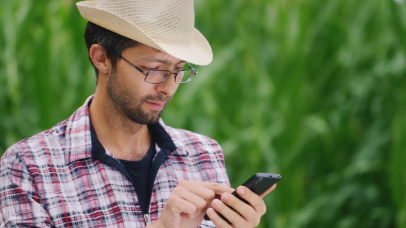 Attractive Farmer With Glasses and Hat is Typing on the Smartphone
