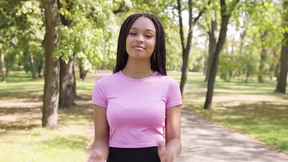 A Young Black Woman Applauds To the Camera and Nods with a Smile in a Park on a Sunny Day