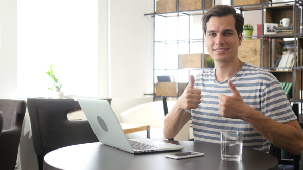 Both Hands Thumbs Up by Creative Man at his Workplace