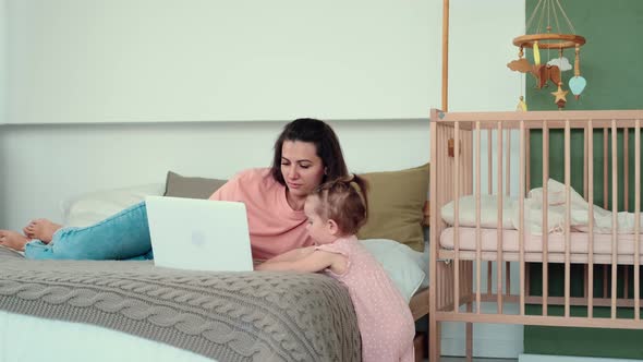 Mom Works Using Laptop While Lying on Bed with Baby