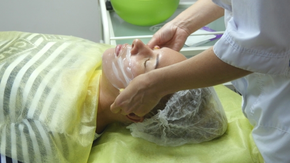 Beautician Applying Facial Mask On a Beautiful Girl Face At Beauty Salon. Woman Having a Facial Care