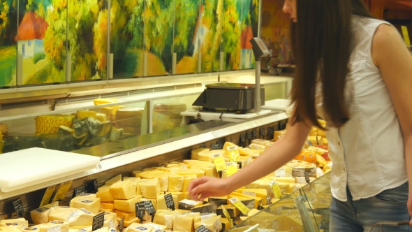 Young Woman With Shopping Cart Coming Up To The Fridge In Shop And Taking Product From It. Girl