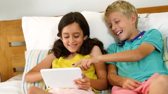 Siblings using digital tablet in bedroom