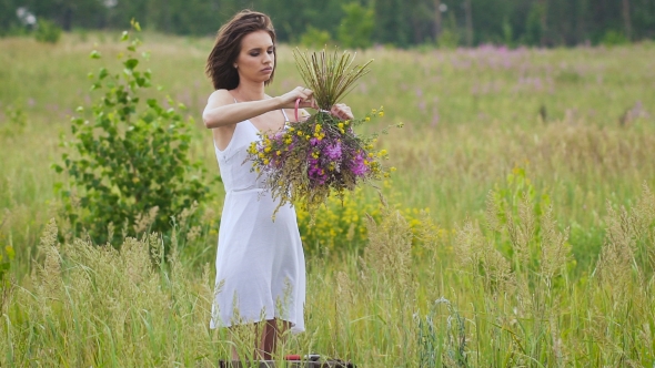 One Young Woman Winding a Flower Bunch Standing On Green Field