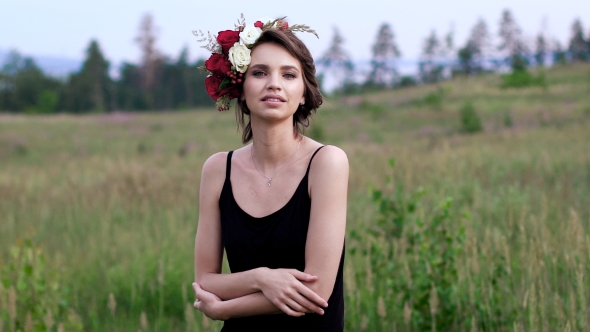 Beautiful Girl In The Black Short Dress With The Wreath On Her Head On The Green Field.