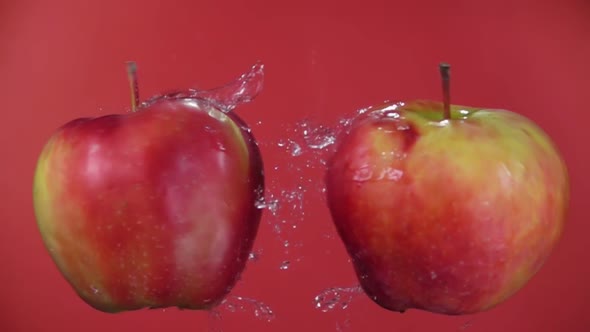 Closeup of Apples Colliding and Splashing Drops of Water on a Red Background