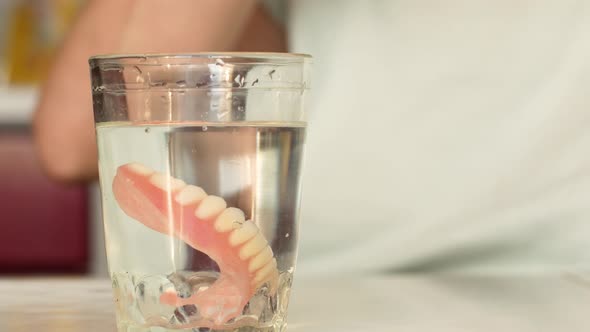 Close-up of a woman taking off her dentures and putting them into a glass of water.