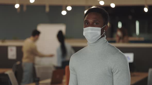 Young African American Handsome Businessman in Medical Mask Looking at the Camera Standing in Modern