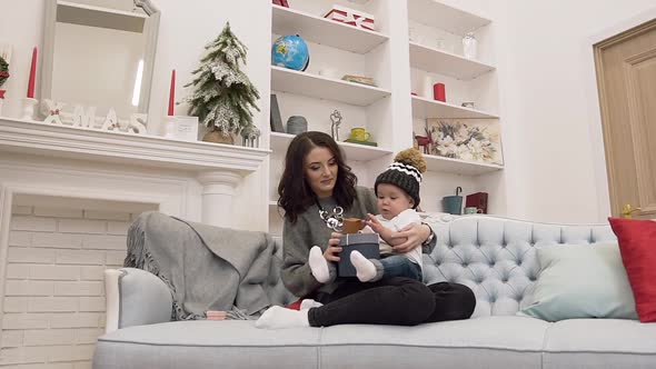 Little Baby Sitting with Her Smiling Pretty Mother on the Sofa