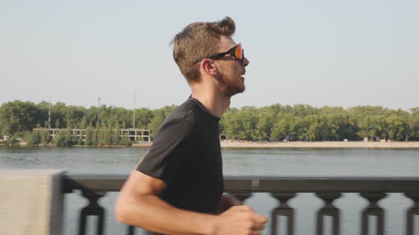 Portrait of young handsome bearded athlete running at sunset along city river training for race