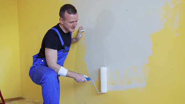 Young man painting wall with roller brush while renovating his apartment