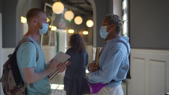 Happy University Students Greeting in Lobby and Elbow Bumping While Wearing Protective Face Masks.