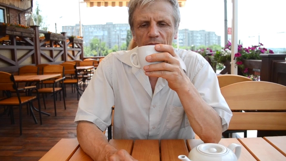 Older Man Sitting At Table And Drinking Tea Outdoors
