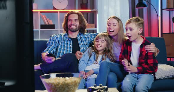 Family Gethering Together in front of TV set in the Evening to Watch Comedy or Entertaining Show