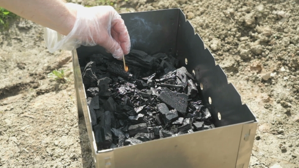 Hand With a Burning Match Ignites The Charcoal