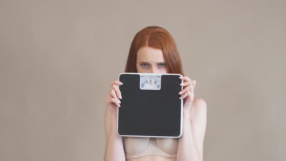 Anorexic Girl with a Sad Face Holds the Scales and Looks at Camera.