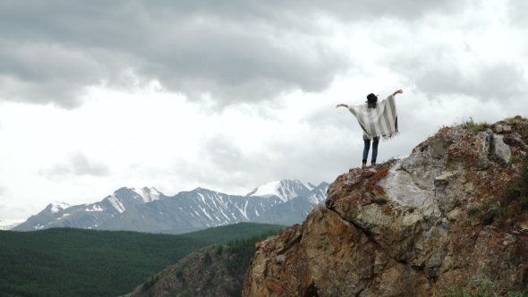 Young Beautiful Woman Traveler Wearing Hat And Poncho Relaxing On The Top Of The Hill With Mountains