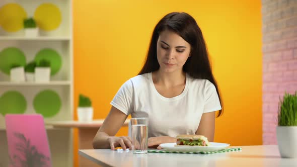 Pretty Female Taking Pill With Water Sitting in Fast Food Restaurant, Overeating