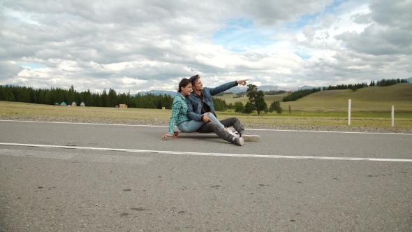 Best Friends Having Fun With Skateboard On Open Road. Young Man And Woman Longboarding Together