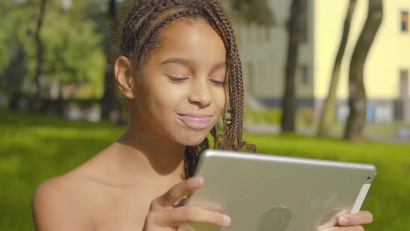 Close-up Portrait of Beautiful Little African American Girl Using Tablet on Sunny Day in Park