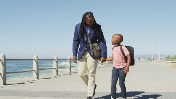 Video of happy african american father and son walking and talking by sea