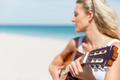 Beautiful young woman playing guitar on beach - PhotoDune Item for Sale