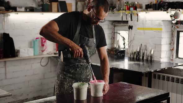 A male handyman mixes paint in a can in a workshop. A sculptor mixes resin with paint to a vase.