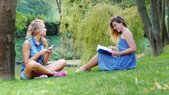 Two Female Friend Relaxing In The Park - Uses The Phone, Read a Book