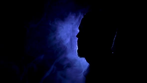 Silhouette of a man on the dark background with blue light and smoke around.