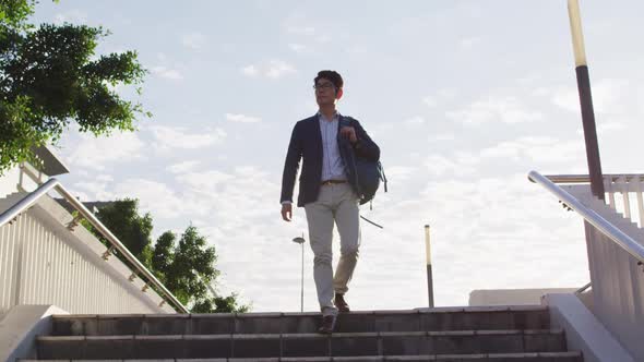 Asian man with backpack walking down the stairs at corporate park