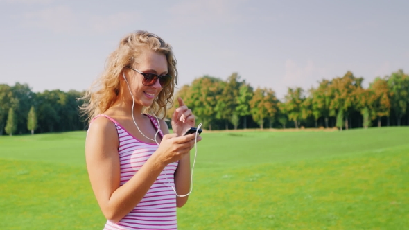Young Woman Goes Near a Large Golf Course, Listening To Music On Headphones