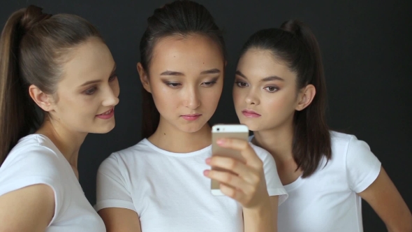 Three Girls Watching Photos On Smartphone In Studio