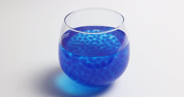 Growing Blue Hydrogel Balls In A Glass Of Water Against White Background