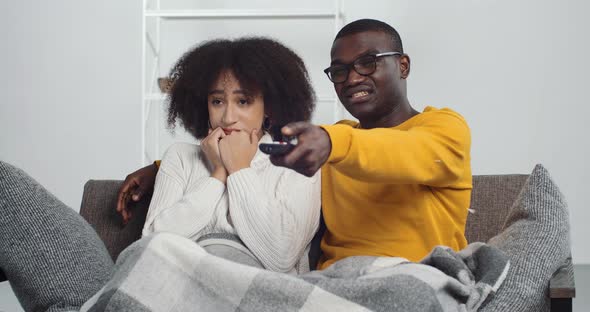 Young Black Guy and African American Girl Sitting on Couch at Home Watching Horror Movie, Curly