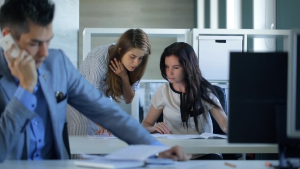 Office Real Estate Company, Man On Phone, In Background Two Young Beautiful Women To Discuss Plan Of