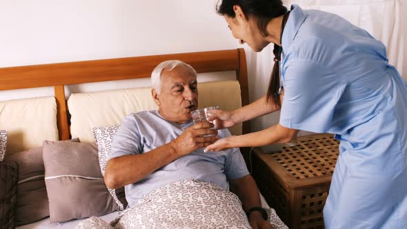 Nurse giving a glass of water to senior man in bedroom