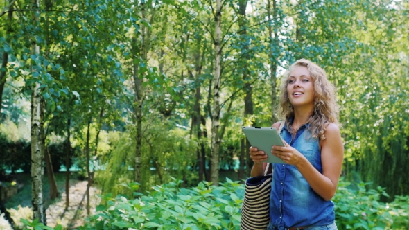 Attractive Woman Walking With a Tablet in the Park, Looking at the Map